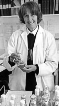 Smiling woman in white lab coat holding a bottle with liquid in it (black and white photo)
